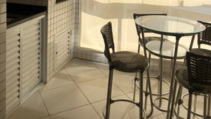 Une cuisine avec des carreaux blancs, un plafond en bois et une fenêtre avec un store. On y trouve deux chaises et une table.