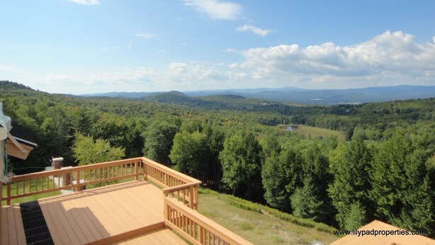 Una terrazza in legno con vista su una valle boscosa e montagne lontane.