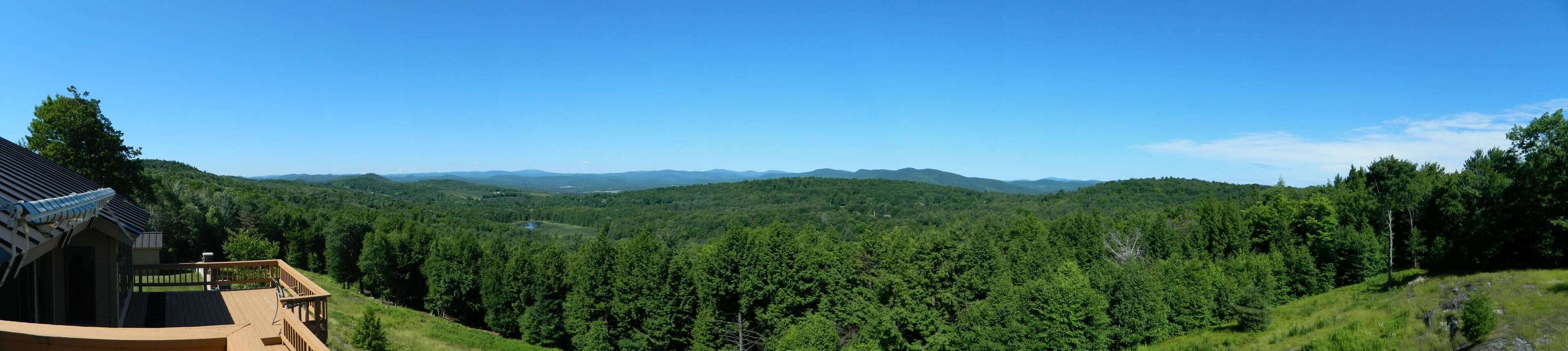 A view of a forested landscape with a building featuring a wooden deck and a sloped roof.