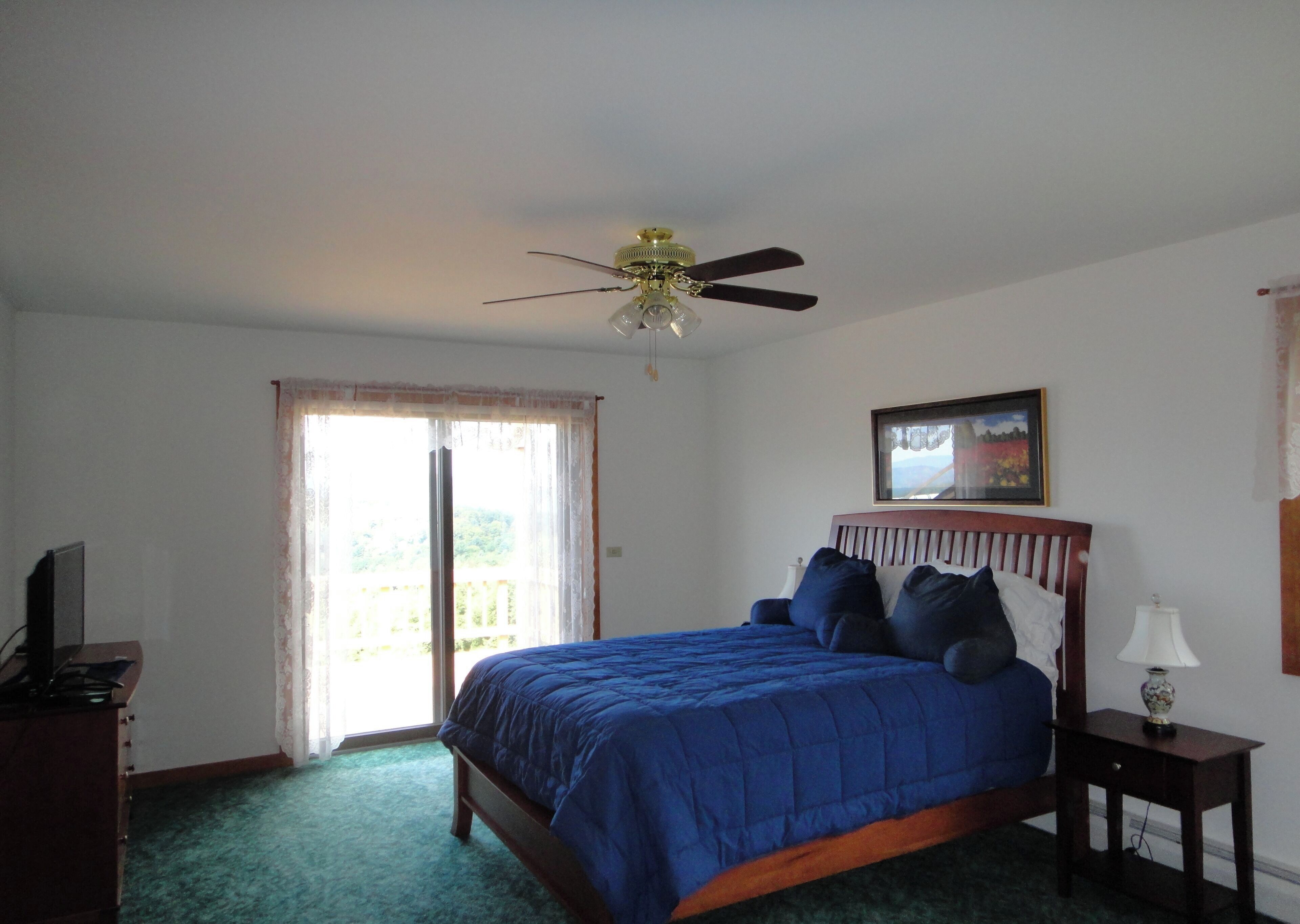 Une chambre à coucher avec un lit, un ventilateur de plafond, une fenêtre, un tableau au mur et une table de chevet avec une lampe.