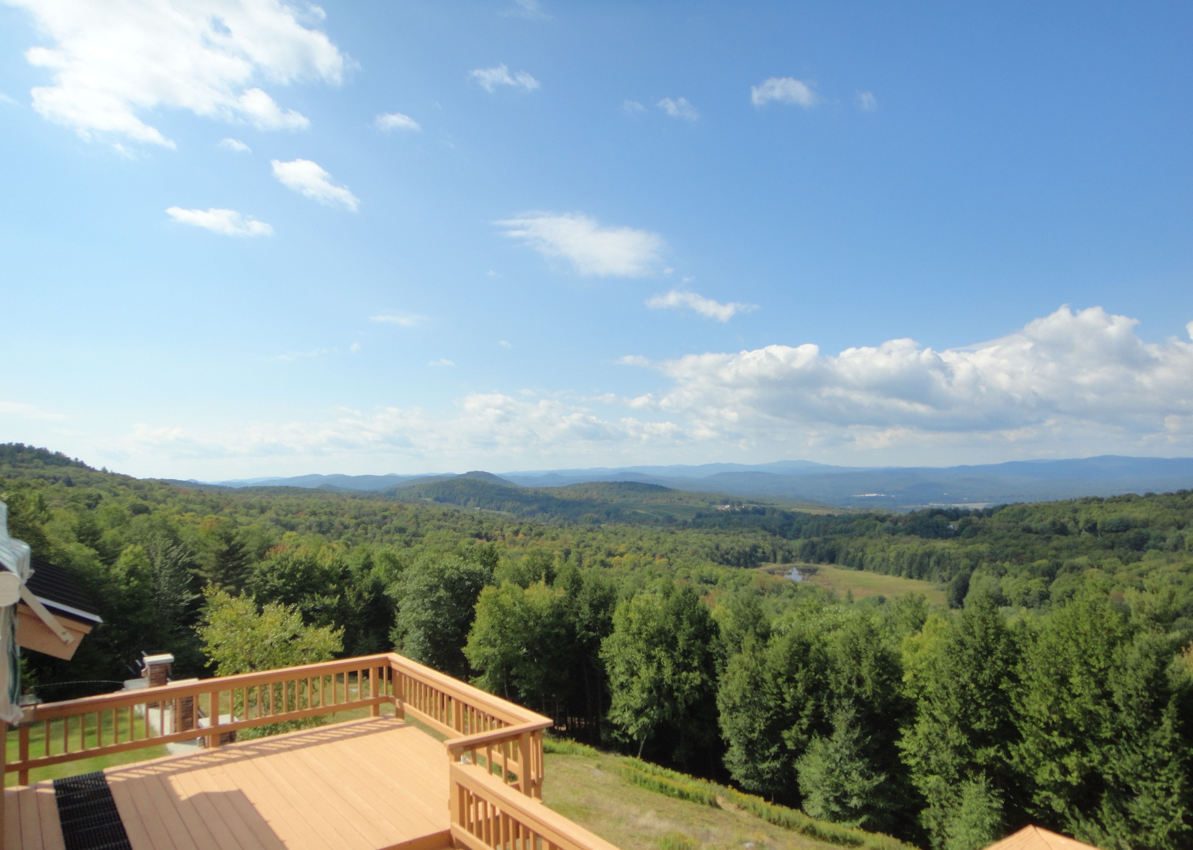 Une terrasse en bois offrant une vue sur une vallée boisée et des montagnes lointaines.