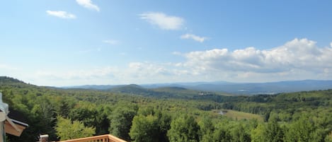 A wooden deck with a view of a forested valley and distant mountains.