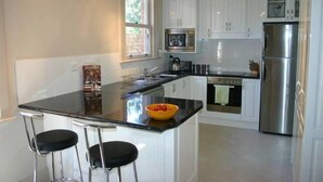 Una cocina moderna con armarios blancos, un refrigerador de acero inoxidable, un microondas y una estufa. Hay dos taburetes de bar con asientos negros.