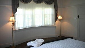 Una habitación de hotel con una cama, dos lámparas de noche, una ventana con cortinas y una puerta.