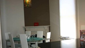 Comedor con una mesa preparada para cuatro, sillas blancas y una caja roja sobre la repisa.