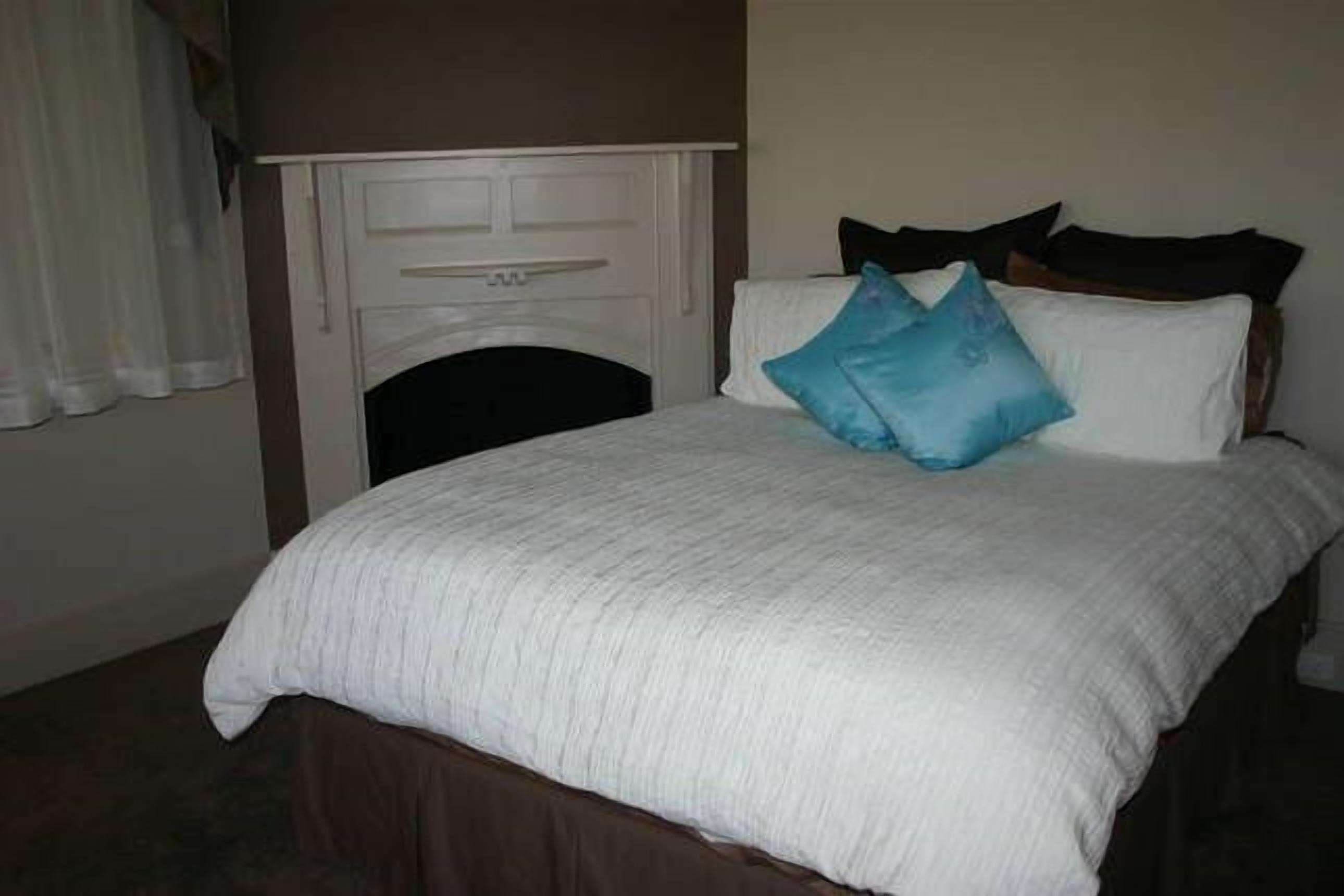 A neatly made bed with a white comforter and two pillows, a white fireplace, and a dark brown headboard.