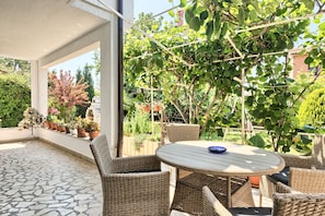 A covered patio with wicker furniture, potted plants, and a view of the garden.
