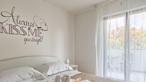A hotel room with a bed, a nightstand, a wall with a 'Always Kiss Me goodnight' sign, and a view of the outside through a sliding door. - Holiday apartment in village Valbandon, 1km from the beach (Valbandon, Fažana)