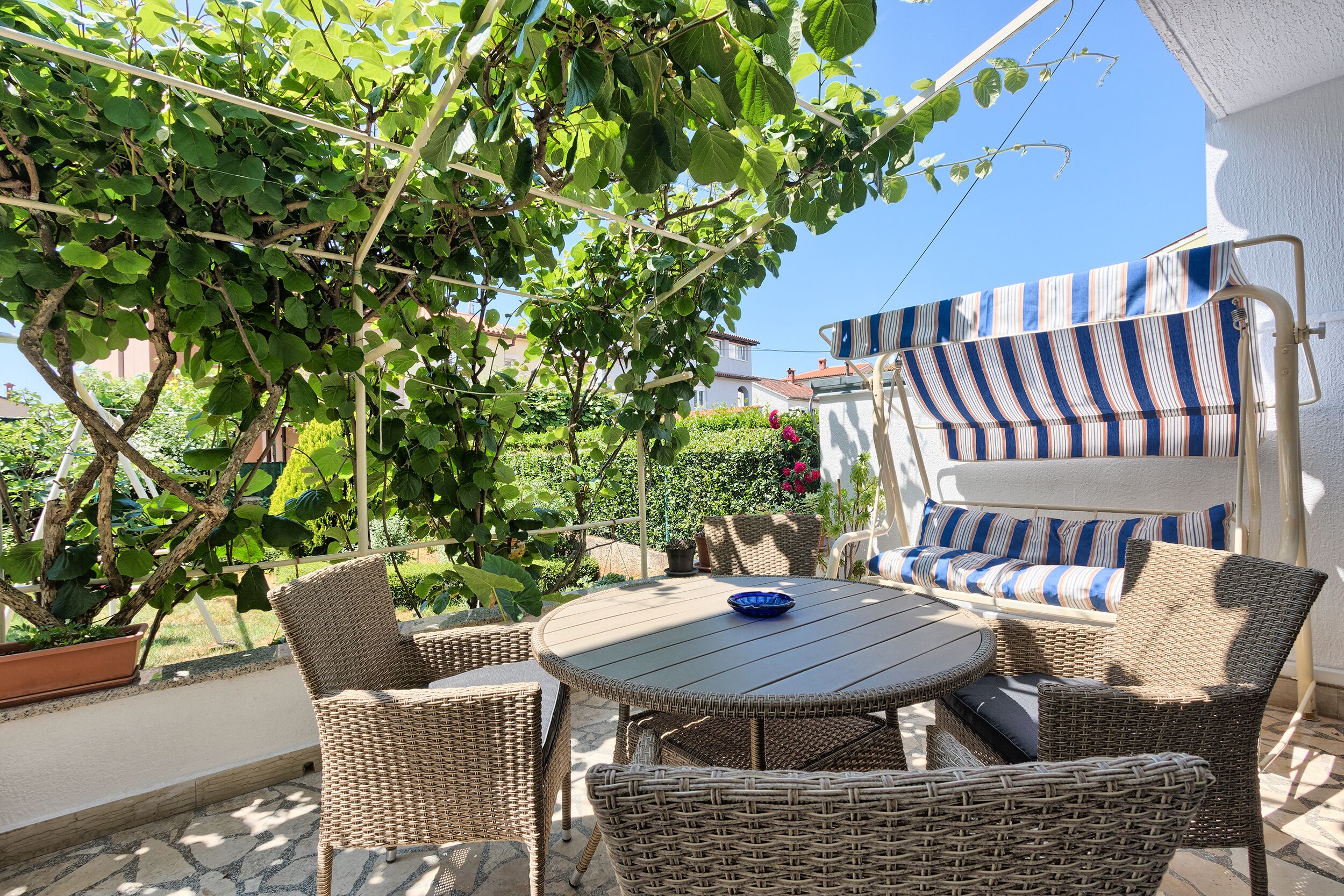 A patio with wicker furniture, a striped awning, and a potted plant.
