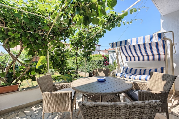 A patio with wicker furniture, a striped awning, and a potted plant.