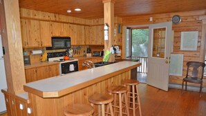 Interior de una cabaña de madera con cocina que incluye estufa, microondas y taburetes de bar.