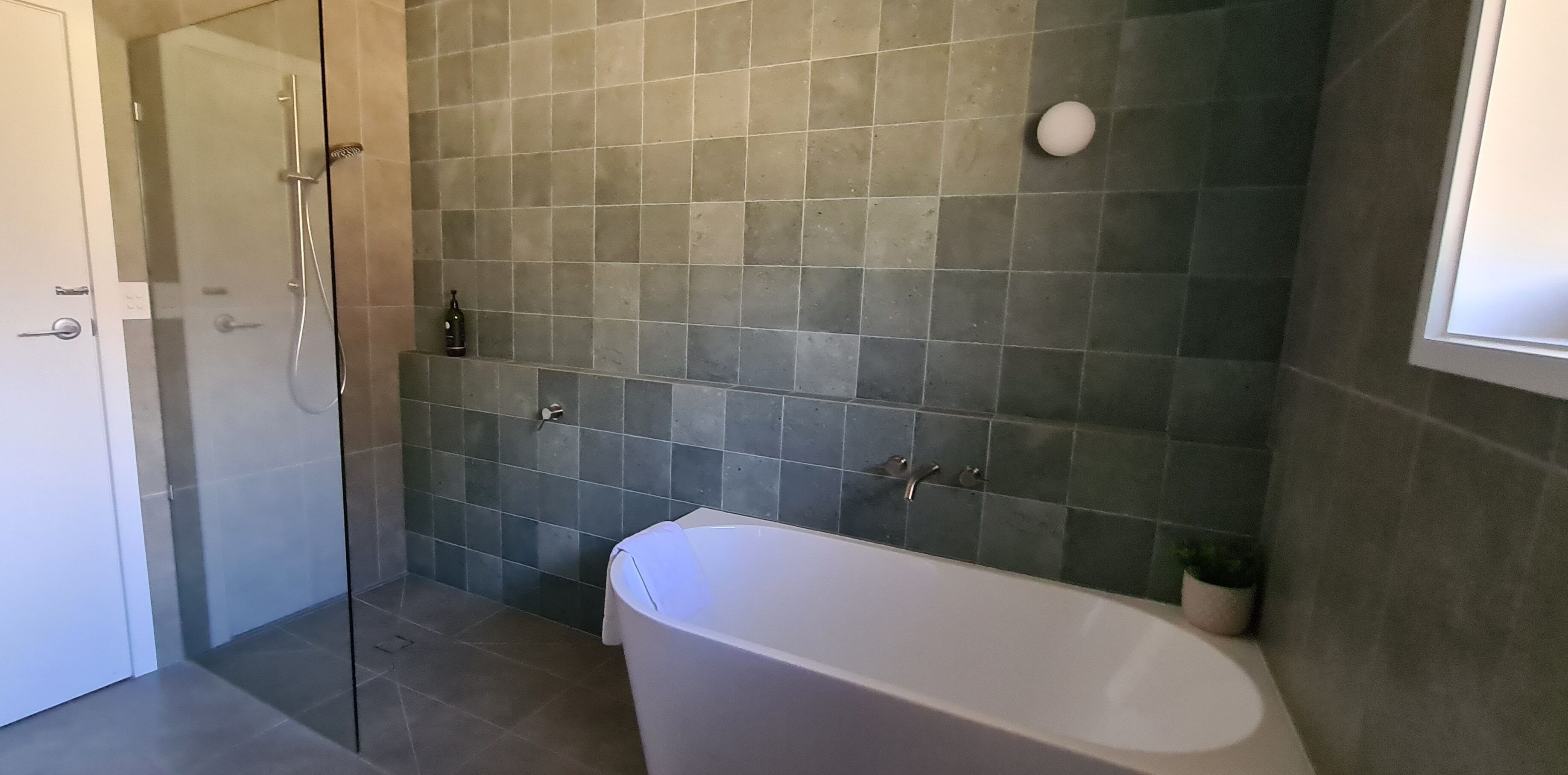 A bathroom with a glass shower enclosure, a white bathtub, and a tiled wall.