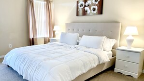 A neatly made bed with white bedding, a headboard, two bedside tables with lamps, and a wall-mounted artwork.