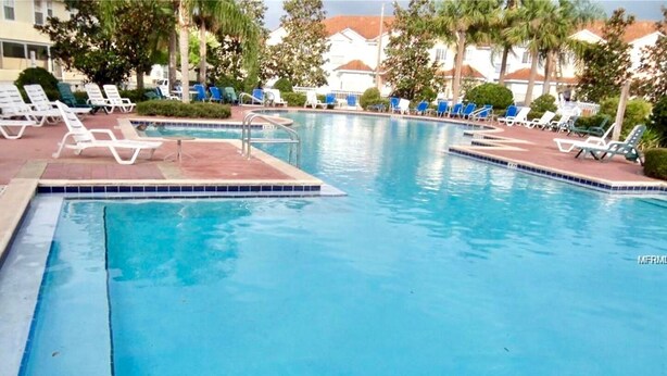 A swimming pool with lounge chairs and a tiled deck.