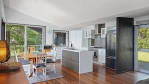 A modern kitchen with a central island, white cabinetry, stainless steel appliances, and large windows offering a view of greenery.