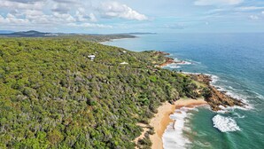 An aerial view of a coastal area with dense greenery, a beach, and a few buildings.