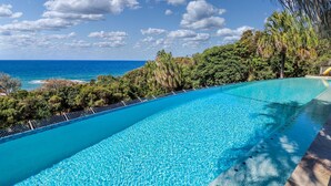A clear blue infinity pool with a view of the ocean and lush greenery.