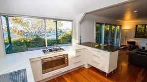 A modern kitchen with a large window overlooking a deck and trees. - NICK'S PLACE - ON BEACH HOLIDAY HOUSE (AGNES WATER)