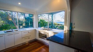 A modern kitchen with white cabinets, a stainless steel sink, and a gas stove. - NICK'S PLACE - ON BEACH HOLIDAY HOUSE (AGNES WATER)