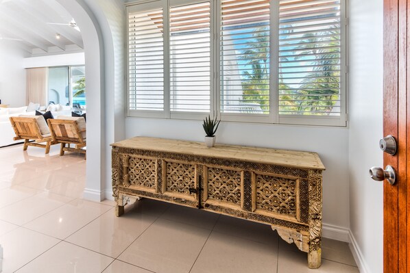 A wooden console table with intricate carvings, positioned against a wall with large windows and a door.