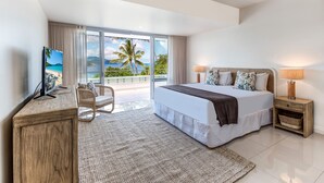 Un dormitorio moderno con una cama grande, televisión, una silla y vista a la playa.