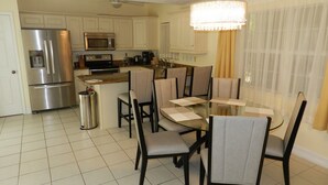 Een moderne keuken met roestvrijstalen apparatuur, een eethoek met een glazen tafel en stoelen, en een kroonluchter.