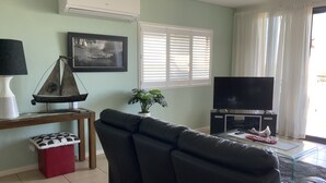 Un salon avec un canapé, un téléviseur, une table avec une lampe, un tableau encadré et une plante en pot.
