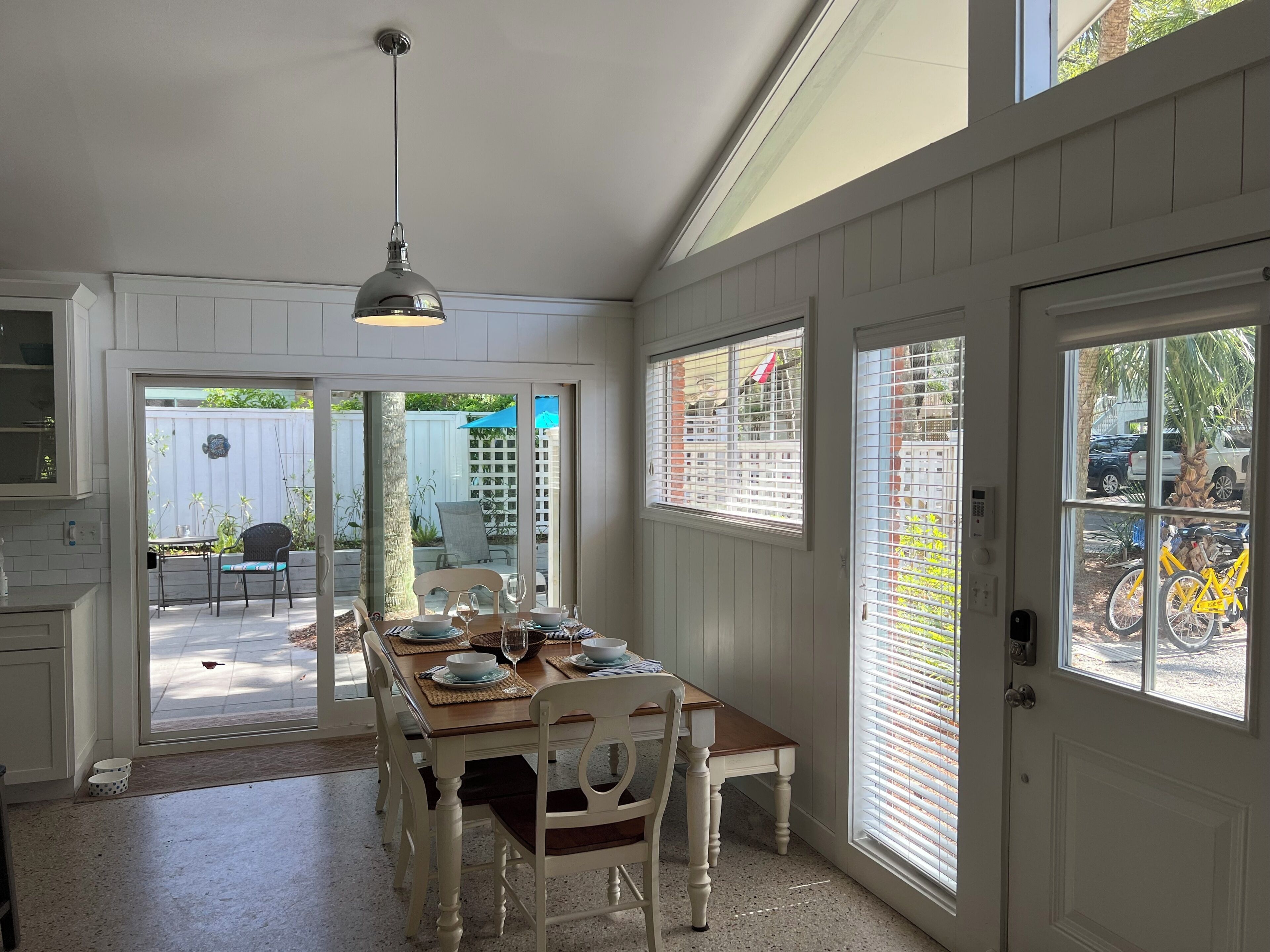 A dining area with a wooden table and chairs, a pendant light, and a view of the backyard through glass doors.