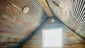 Un dormitorio abrigado en el desván, con dos camas, paredes de madera, un ventanal pequeño y techo inclinado.