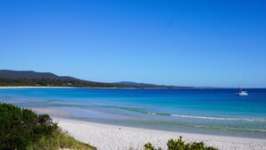Ein Strand mit klarem, blauem Wasser, weißem Sand und Segelbooten.