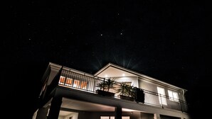Ein zweistöckiges Haus mit Balkon, großen Fenstern und einer gut beleuchteten Fassade bei Nacht.