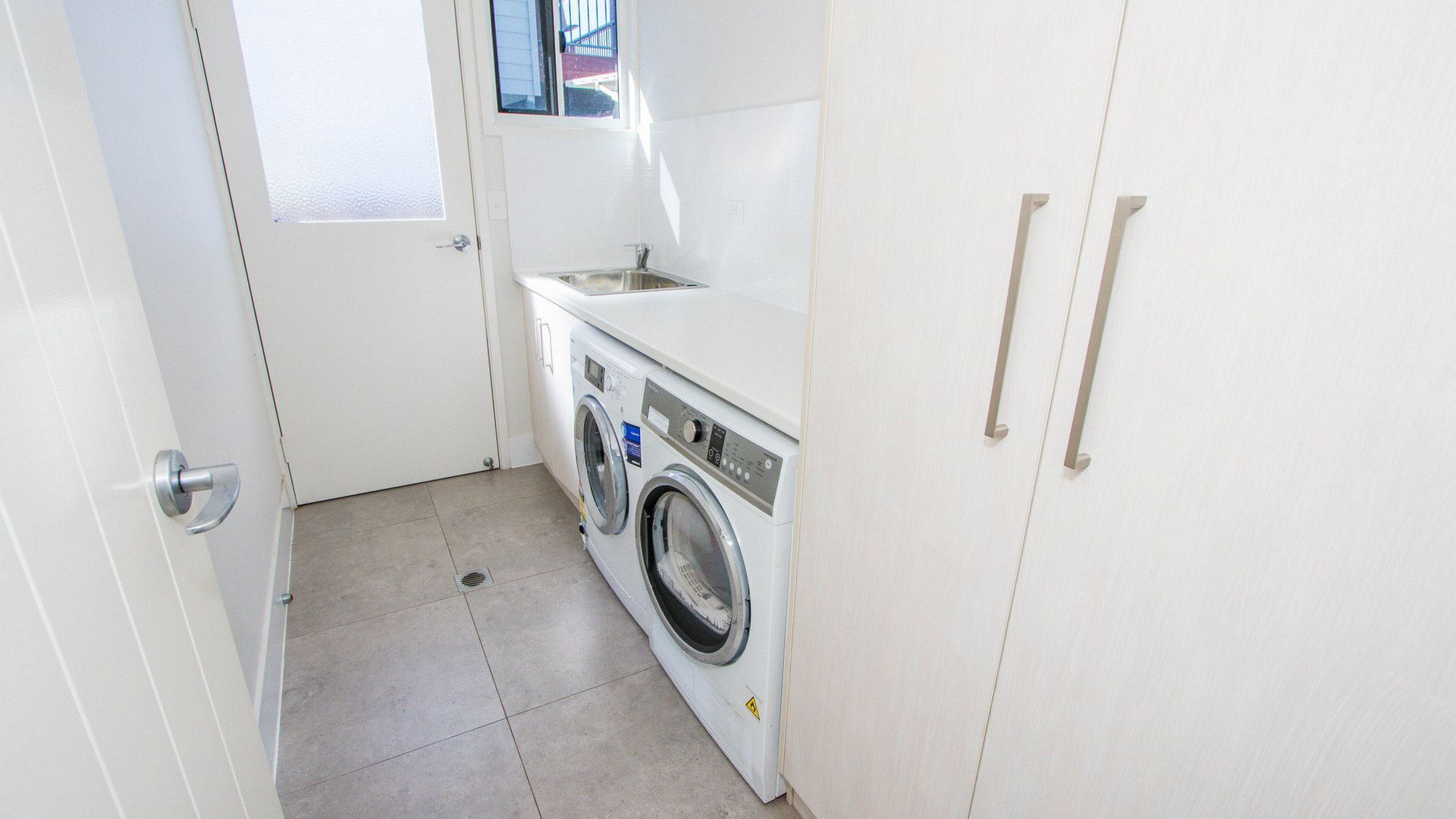 A compact laundry room with a washing machine, a sink, and a door with a window above it.