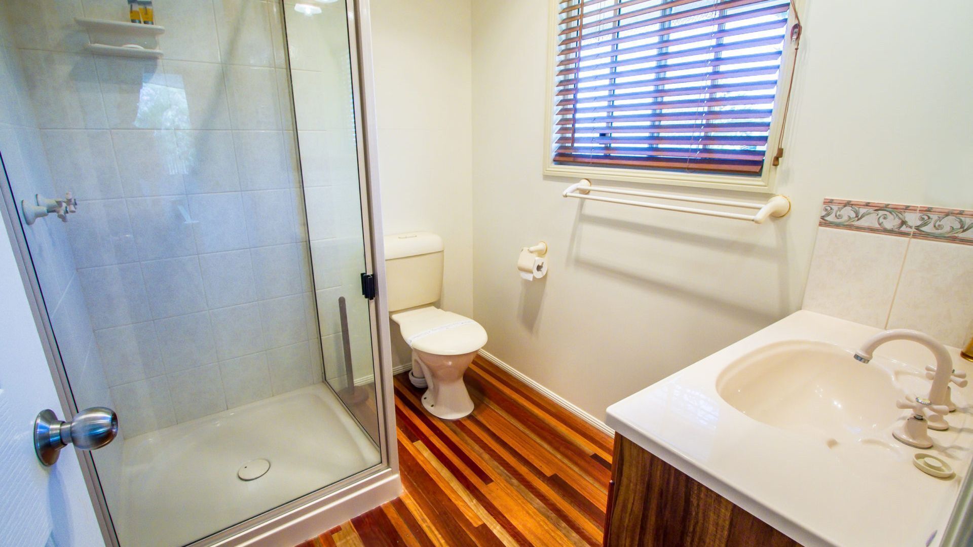 A bathroom with a glass shower enclosure, a toilet, and a sink with a mirror.