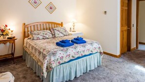 Un dormitorio con cama de madera, ropa de cama floral, una mesita de noche con lámpara y una puerta a la derecha.