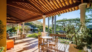Eine Terrasse im Freien mit Holzmöbeln, gefliestem Boden und Blick auf einen Hügel.