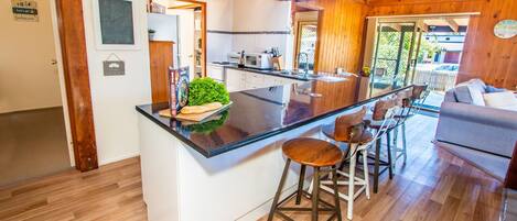 Una cocina con una isla central, taburetes de bar, un comedor con sofá y vistas al exterior.