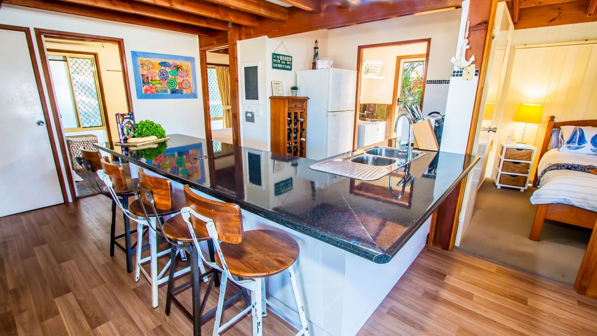 A kitchen with a bar area, wooden stools, a refrigerator, a sink, and a dining table.