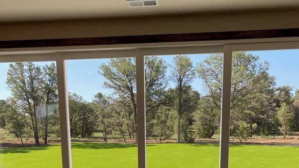 A room with large windows, wooden flooring, and a view of a green lawn and trees. - Popular Vacation Rental At The Grand Canyon, Make yourselves at Home! (Williams)
