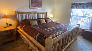 A wooden-framed bed with a patterned bedspread, a ceiling fan, a nightstand with a lamp, and a window with blinds. - Popular Vacation Rental At The Grand Canyon, Make yourselves at Home! (Williams)