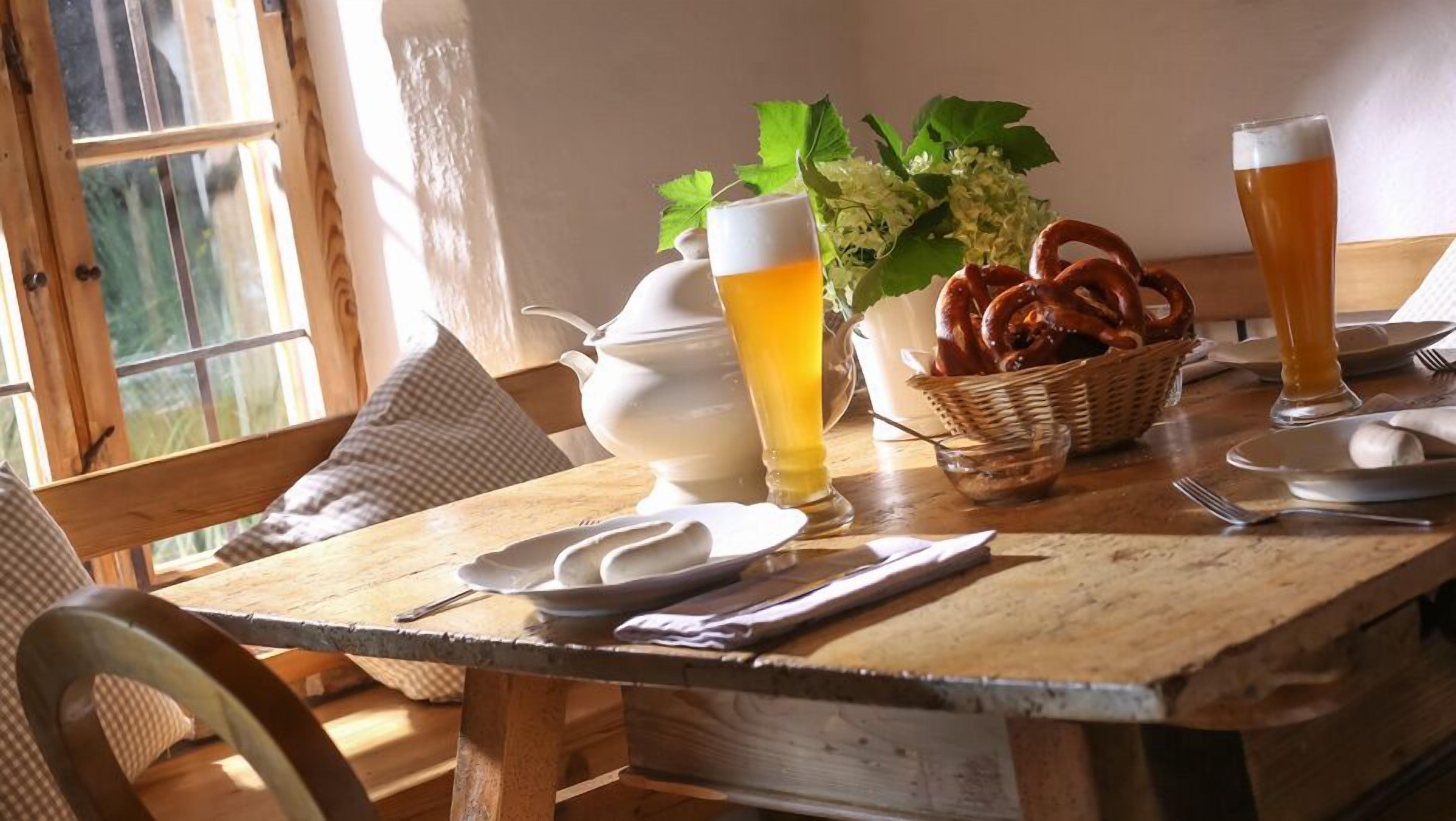 Ein Holztisch mit einer weißen Krug, einem Bierglas, Brezeln und einem Brotkorb.