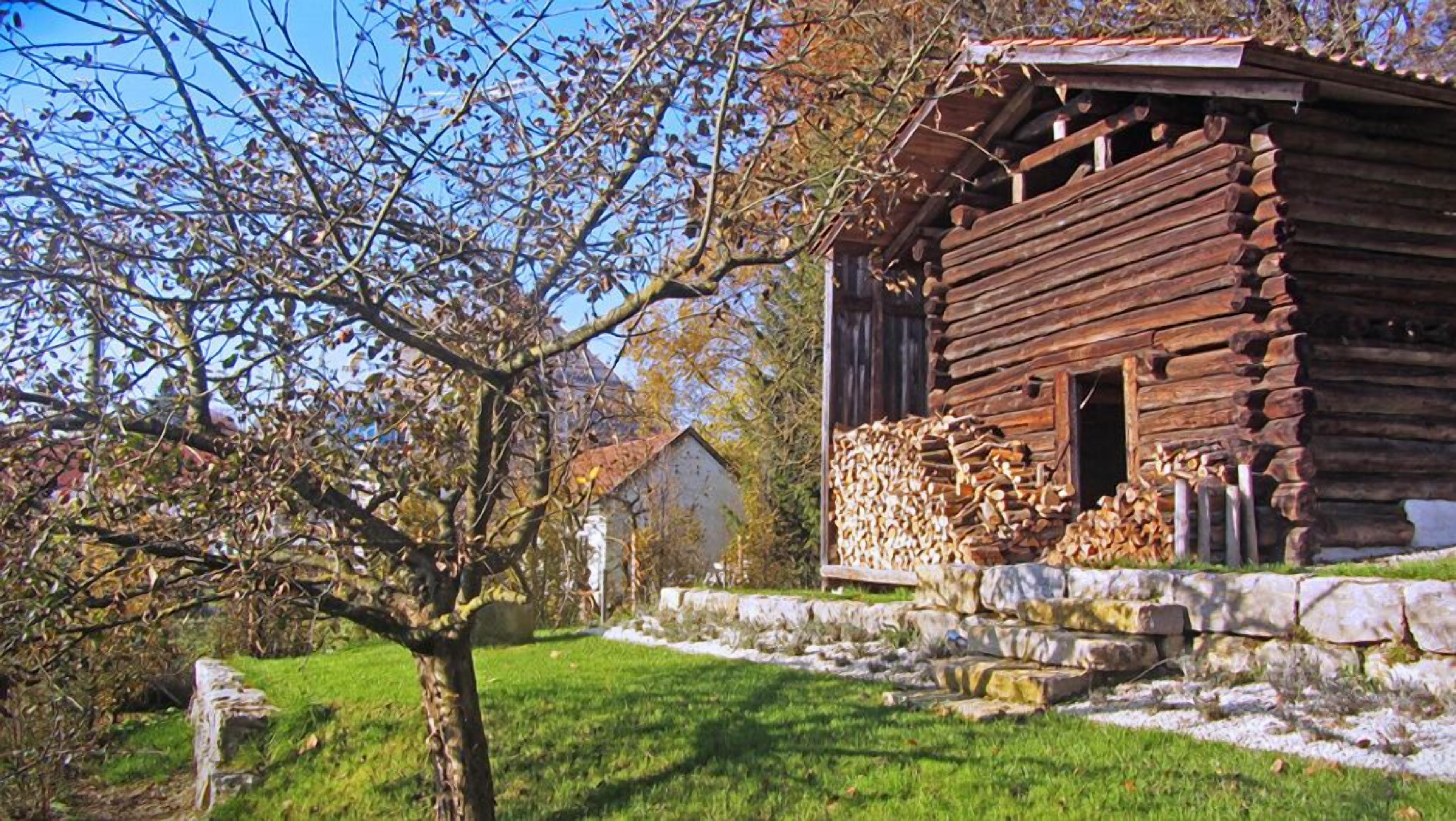 Eine rustikale Blockhütte mit Steinunterbau, einer Holzterrasse und einem Holzstapel davor.