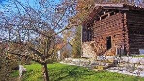 Eine rustikale Blockhütte mit Steinunterbau, einer Holzterrasse und einem Holzstapel davor.