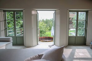 A bedroom with a large window, a wooden hot tub, and a view of greenery. - HISTORIC BAVARIAN COTTAGE; Heritage Stay with Sauna, Hot Tub and Spa (Haag an der Amper)