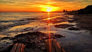 Um pôr do sol sobre uma praia, com troncos de madeira em primeiro plano.