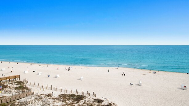 A beach with a wooden boardwalk and white structures, likely beach huts or storage units.