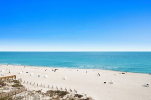 A beach with a wooden boardwalk and white structures, likely beach huts or storage units.