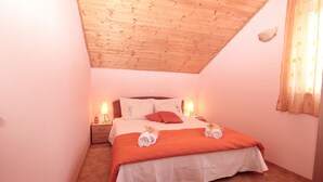 Un dormitorio con techo inclinado, una cama con colcha blanca y naranja, dos lámparas de noche y una mesita de noche con una lámpara.