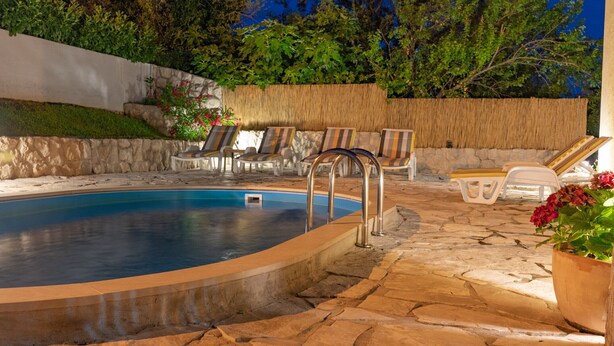 Una piscina con baldosas de piedra, sillas de descanso y una pared de paja.