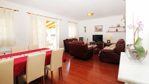 Una sala de estar con comedor, piso de madera, televisor y una mesita con lámpara.
