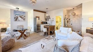 A spacious living room with a white sofa, a coffee table, and a dining area with a wooden table and chairs.